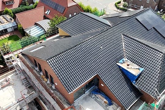 Luftbild eines Mehrfamilienhauses im Umbau: frisch gedecktes Dach, eingerüstete Klinkerfassade