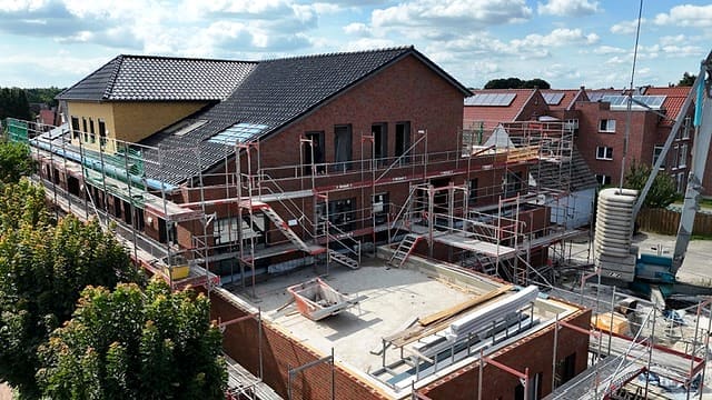 Mehrfamilienhaus im Umbau: eingerüstete Klinkerfassade, das Dach zur Hälfte neu eingedeckt, im Vordergrund die Rohdecke des Anbaus