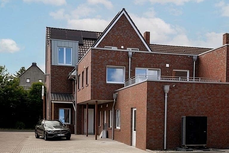 Dasselbe Klinkerhaus nach der Sanierung: neuer Klinkergiebel, metallverkleidete Gaube, offene Dachterrasse und Wärmepumpe am Anbau