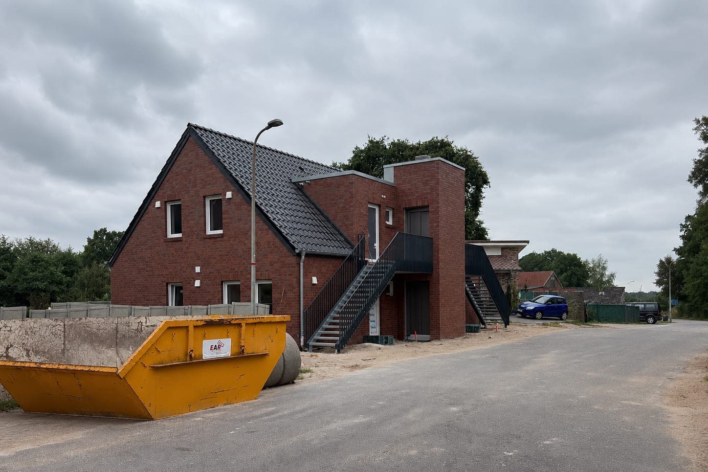 Kurz vor der Fertigstellung: zweigeschossiges Klinkerhaus mit steilem Satteldach, flach gedecktem Treppenturm und zwei Außentreppen