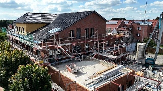 Mehrfamilienhaus im Umbau: eingerüstete Klinkerfassade, das Dach zur Hälfte neu eingedeckt, im Vordergrund die Rohdecke des Anbaus